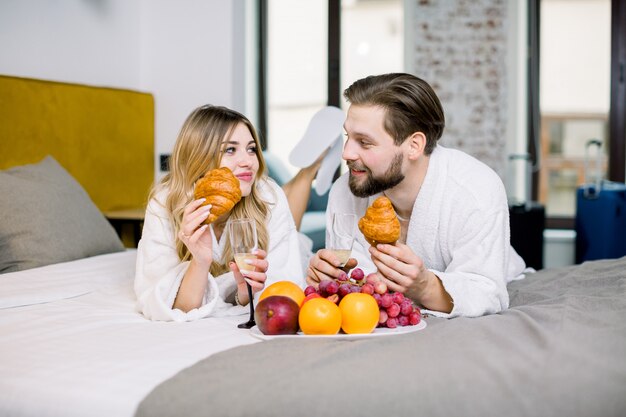 Desfrutando de café da manhã, frutas, croissants, champanhe. Homem mulher, desgastar, roupões branco, café manhã, em, quarto hotel