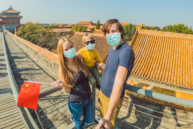 Desfrutando de férias na China família feliz em máscara médica com bandeira nacional chinesa na cidade proibida