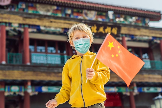 Desfrutando de férias na China, menino com máscara médica com bandeira nacional chinesa no fundo de