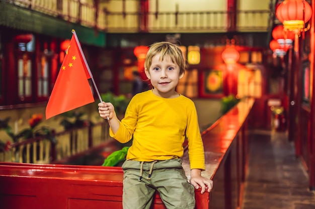 Desfrutando de férias na China Menino turista feliz com uma bandeira chinesa em um fundo chinês Viajar para a China com o conceito de crianças Trânsito sem visto 72 horas 144 horas na China