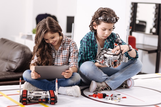 Desfrutando de novos dispositivos. positivo envolveu crianças divertidas sentadas em casa e usando gadgets e dispositivos enquanto se divertiam