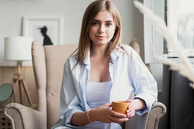 Desfrutando de seu café fresco Linda jovem bebendo café e olhando pela janela enquanto está sentado na poltrona em casa