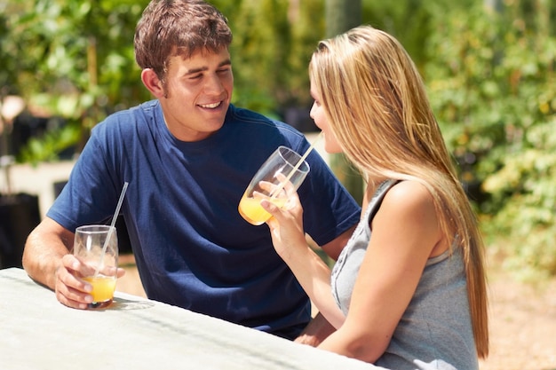 Desfrutando de um encontro tranquilo Um jovem casal sentado do lado de fora e bebendo suco de laranja