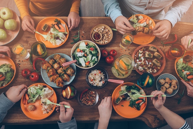 Desfrutando de um jantar com amigos. Vista superior de um grupo de pessoas jantando enquanto estão sentados à mesa de madeira rústica