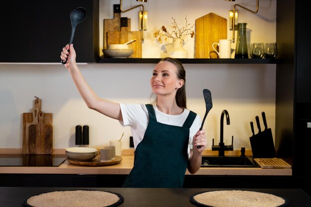 Desfrutando de um maravilhoso novo dia linda jovem em um avental dançando em pé na cozinha em ho