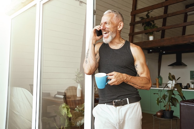 Desfrutando de uma boa conversa, um homem caucasiano de meia-idade feliz falando ao celular e rindo enquanto