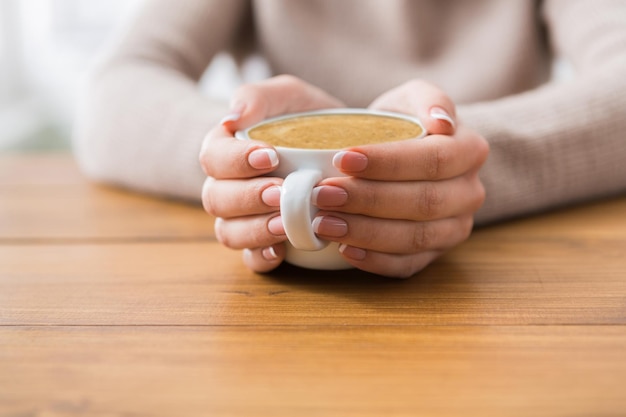 Desfrute de uma xícara de café. Closeup de mãos de mulher com café expresso aromático ou americano na mesa de madeira