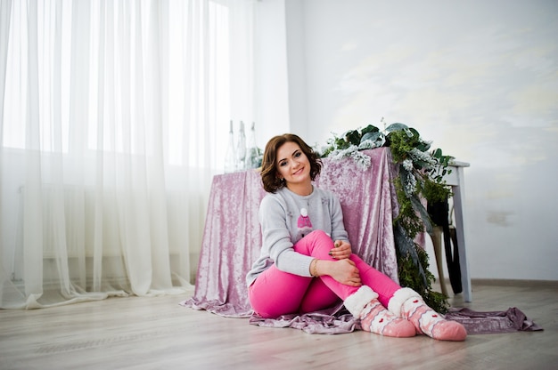 Desgaste da menina na camiseta do inverno que senta-se contra a tabela na sala com decorações dos chrismas.