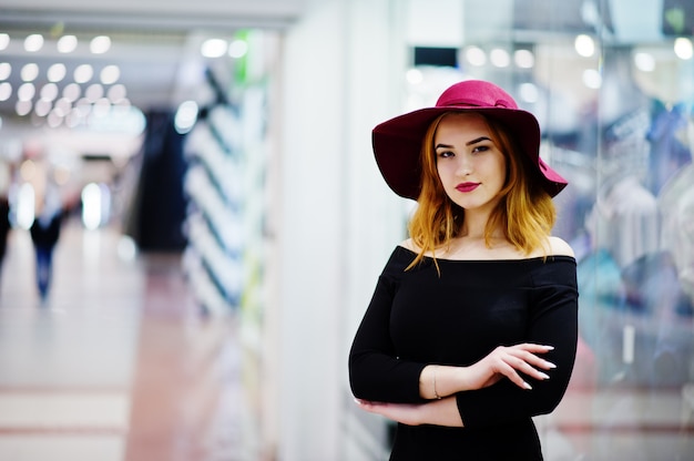 Desgaste de la muchacha pelirroja de la moda en el vestido negro y el sombrero rojo presentados en el centro comercial.