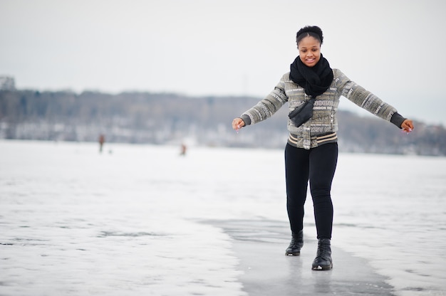 Foto desgaste de la mujer africana en pose de bufanda negra en el lago de hielo congelado, día de invierno en europa.