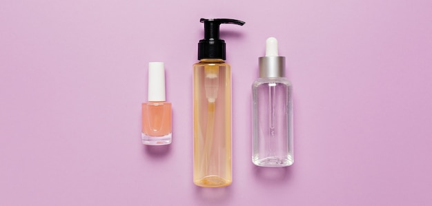 Design de embalagens de cosméticos orgânicos. Posição plana, garrafa de bomba de vidro transparente de vista superior, frasco de escova, frasco de soro hidratante em um fundo roxo. Cosméticos naturais SPA