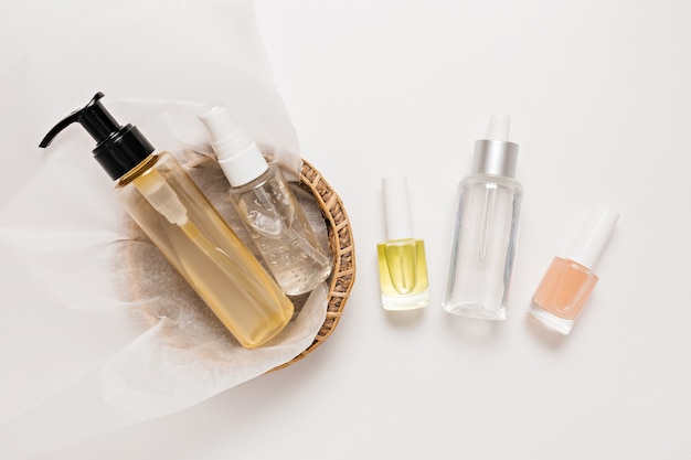 Design de embalagens de cosméticos orgânicos. Posição plana, garrafa de bomba de vidro transparente de vista superior, frasco de escova, frasco de soro hidratante em uma cesta de papel em um fundo branco. Cosméticos naturais SPA