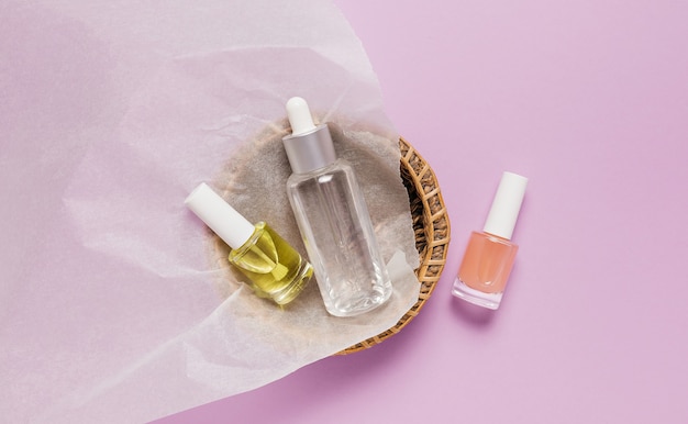 Design de embalagens de cosméticos orgânicos. Posição plana, garrafa de bomba de vidro transparente de vista superior, frasco de escova, frasco de soro hidratante em uma cesta de papel em um fundo roxo. Cosméticos naturais SPA