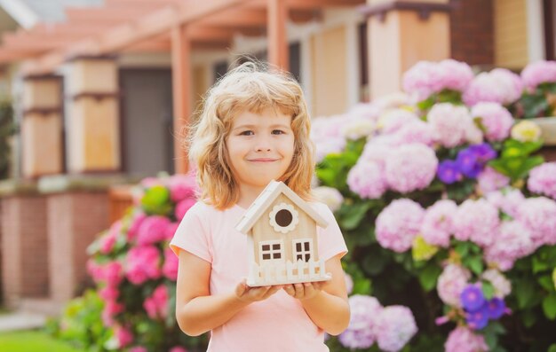 Design Ihres Traumhauskindes, das mit einem kleinen Hausmodell im Freien im heimischen Garten spielt