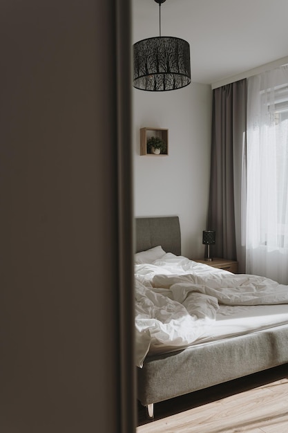 Design interior de quarto estético Neutral escandinavo sala de estar confortável com cama lençóis de cama amassados janela com cortinas sombras de luz solar