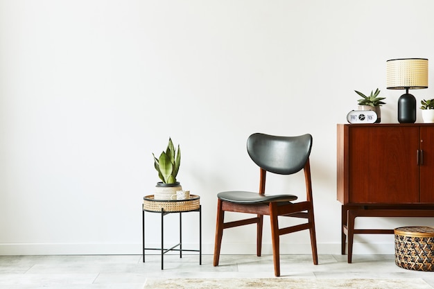 Design interior elegante de sala de estar com cômoda retro de madeira, cadeira, plantas, cesta de vime, decoração, lâmpada, relógio e acessórios pessoais elegantes. Copie a parede branca do espaço. Modelo.