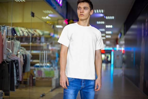 Design Mockup weißes T-Shirt auf dem Hintergrund von Geschäften, Vorderansicht. Vorlage von Kleidung auf einem jungen Mann. Platz für Ihr Muster.