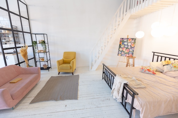 Design moderno e luxuoso de um pequeno apartamento aconchegante de estilo escandinavo com paredes brancas, segundo andar com uma biblioteca e uma grande janela alta cheia de luz do dia