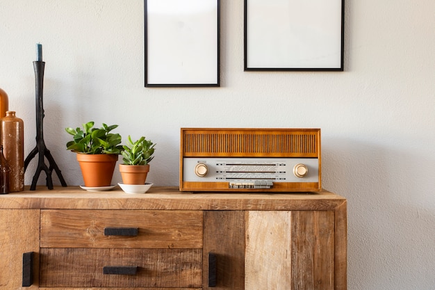 Design retrô da sala de estar com armário e rádio, juntamente com plantas verdes e moldura em branco, parede branca