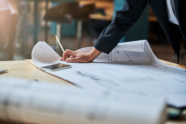 Designer concentrada em pé perto da mesa enquanto olhava para o esboço, pensando em seu projeto