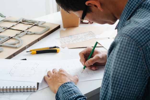 Designer de caixa focado fazendo um esboço no papel com um lápis curvado Sentado atrás da mesa desenhando