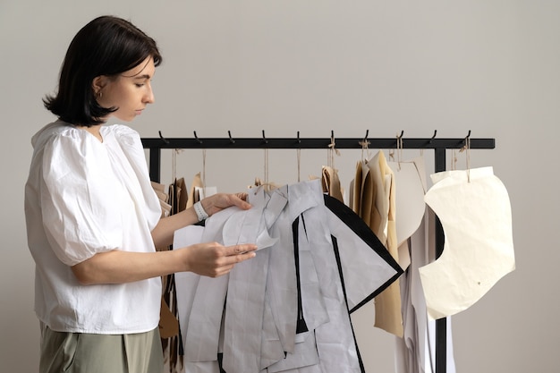 Designer de moda ou costureira profissional pendura padrões de papel artesanal em cabides no ateliê