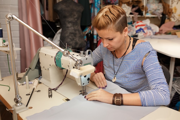 Designer de pano jovem costureira loira feminina trabalha na máquina de costura