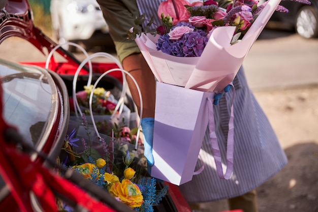 Designer floral colocando um ramo de flores caindo dentro de uma embalagem de papel roxo no porta-malas de um carro