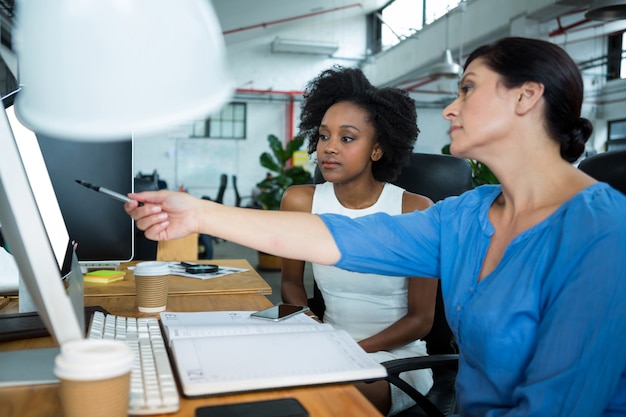 Designer gráfica feminina apontando para um PC de mesa