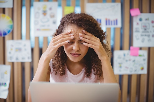 Designer gráfica feminina frustrada com laptop sentado na mesa