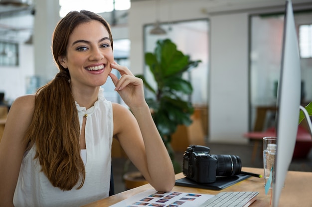 Designer gráfica feminina sorridente, sentada à mesa