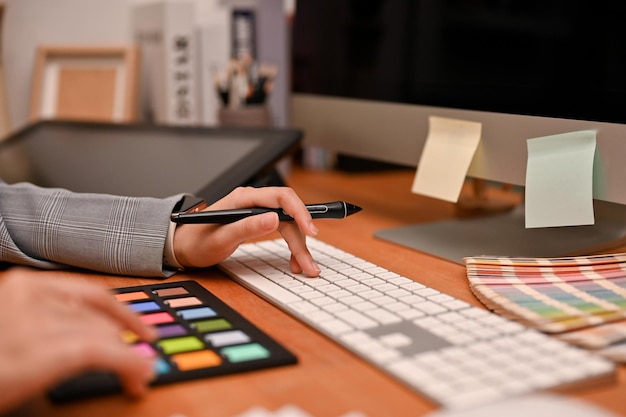 Foto designer gráfico feminino segurando uma caneta digitando no teclado do computador