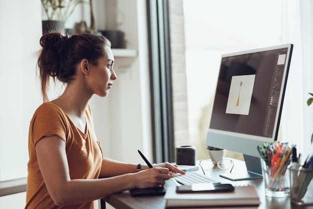 Designer jovem trabalhando no computador de seu escritório em casa.