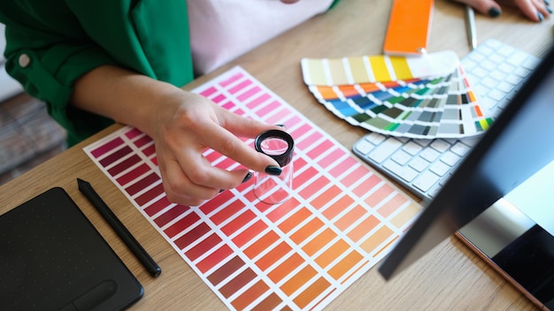 Designer mit Lupe arbeitet mit Pantone-Skala im Computer-Zeichentablett des Kunststudios