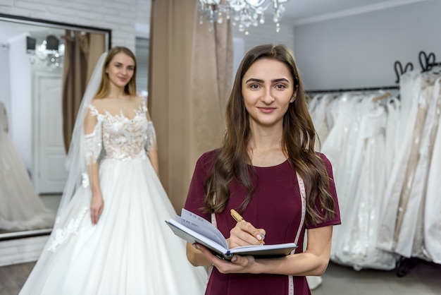 Designer mit Notizblock und Braut im Hochzeitskleid dahinter
