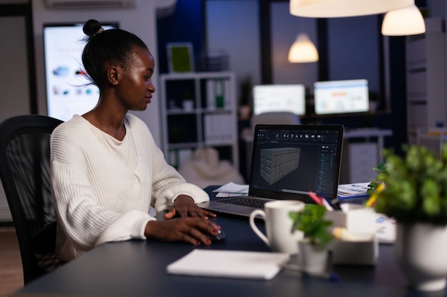Designer, mulher negra, engenheira, olhando para laptop, analisando projeto usando um novo software para projetar o conceito 3D de contêiner trabalhando horas extras em uma empresa iniciante para protótipo