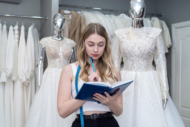 Designer ou vendedor muito feminino fazendo anotações perto do vestido na loja de moda de casamento