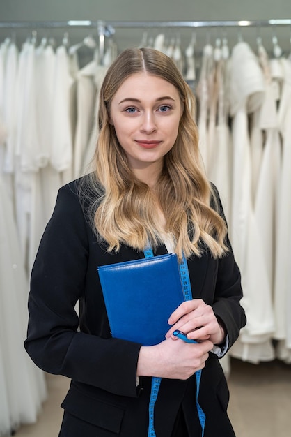 Designer ou vendedor muito feminino fazendo anotações perto do vestido na loja de moda de casamento