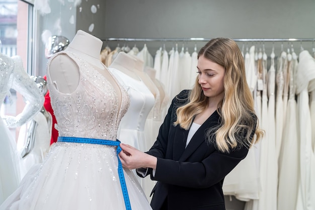 Designerfrau mit Maßband misst Hochzeitskleid auf Schaufensterpuppe