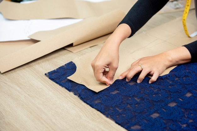 Designerhände, die Papiermuster auf Gewebe am Tisch feststecken