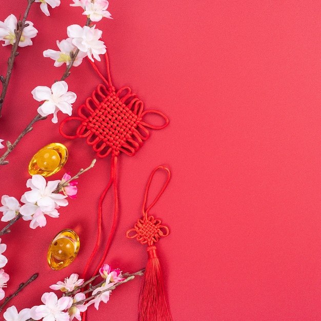 Designkonzept des chinesischen Mondneujahrs Schöner chinesischer Knoten mit Pflaumenblüte isoliert auf rotem Hintergrund flach lag Draufsicht Overhead-Layout