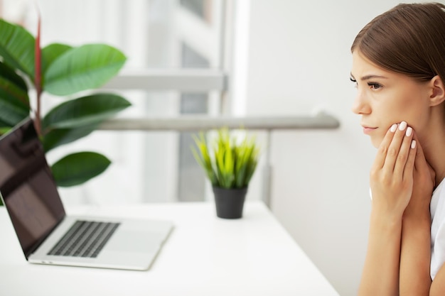 Desillusionierte Dame, die bei der Arbeit im Büro Zahnschmerzen verspürt