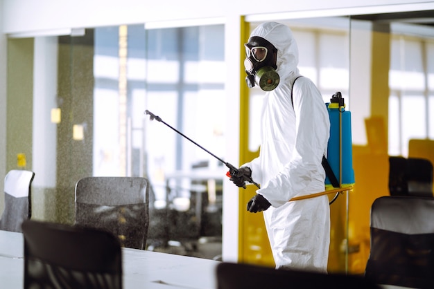 Desinfecção de escritório para prevenir COVID-19, Homem em traje de proteção de materiais perigosos com produtos químicos em spray.