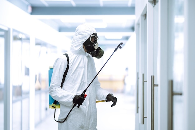 Desinfecção do escritório para prevenir COVID19 Homem em traje de proteção com produtos químicos em spray