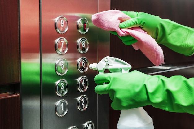 Desinfecção e cuidados higiênicos com álcool spray no botão do elevador.