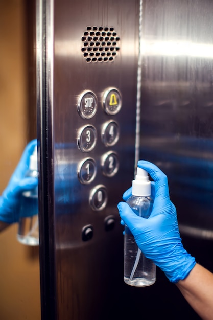 Desinfección de botones en el ascensor con spray antiséptico. Concepto de higiene y protección contra virus.