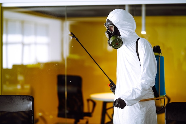 Desinfección de la oficina para prevenir COVID-19, Hombre en traje protector de materiales peligrosos con productos químicos en aerosol.