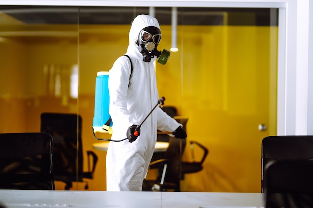 Desinfección de la oficina para prevenir COVID-19, Hombre en traje protector de materiales peligrosos con productos químicos en aerosol.