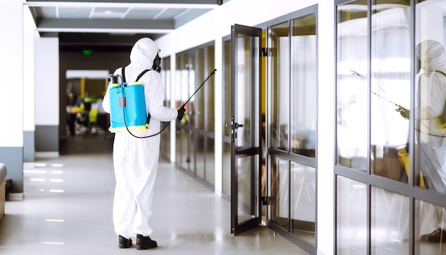 Desinfección de la oficina para prevenir COVID-19, Hombre en traje protector de materiales peligrosos con productos químicos en aerosol.