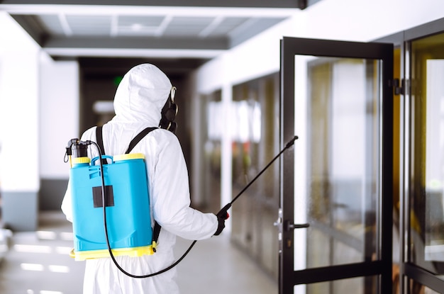 Desinfección de la oficina para prevenir COVID-19, Hombre en traje protector de materiales peligrosos con productos químicos en aerosol.